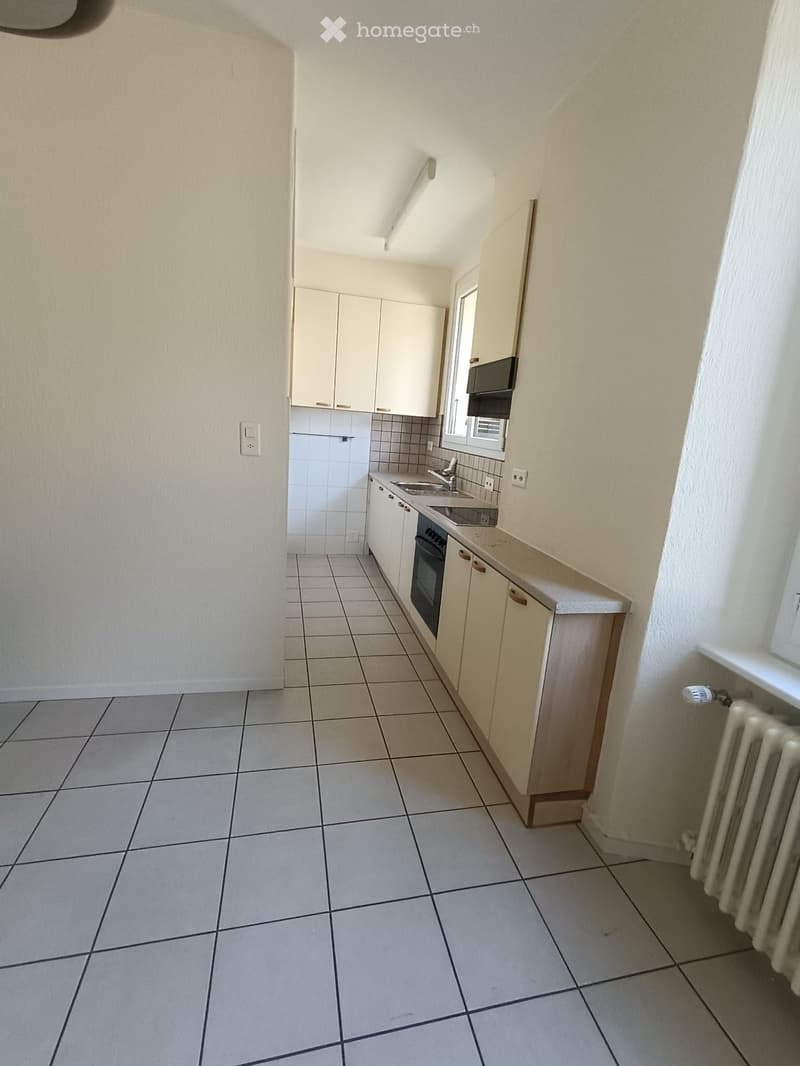 Empty kitchen with tiled floor, white cabinets, sink, oven, and radiator.