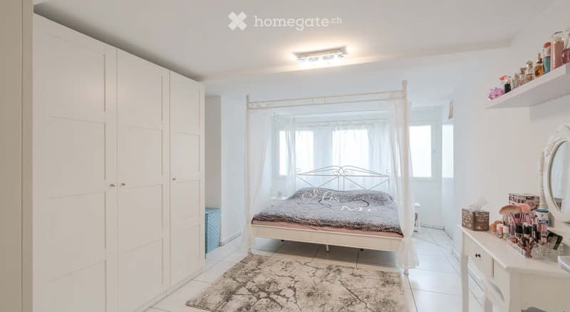 Bedroom. Bright bedroom with a white four-poster bed, vanity with makeup items, shelves, and a patterned rug.