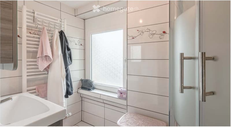 Bathroom. Modern bathroom with white tiles, a sink, toilet, shower, towel rack with towels, and a small shelf holding a handbag and cup.
