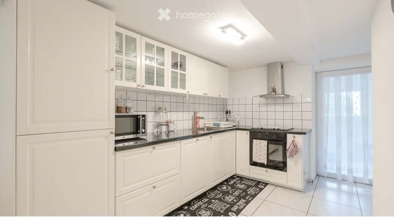 Kitchen. Modern kitchen with white cabinets, stainless steel appliances, and a black countertop. Features include a microwave, oven, sink, and a decorative kitchen mat on the floor.