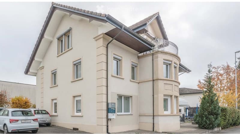 Three story house with beige walls and windows, brown roof, balcony on the second floor