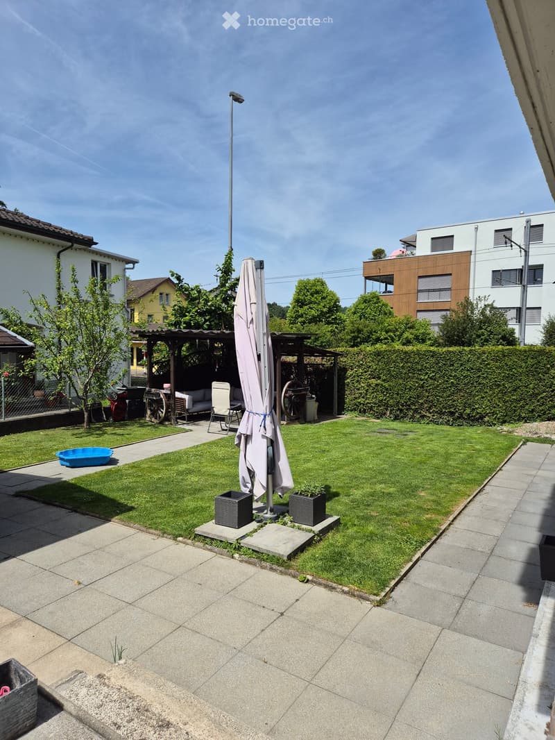 Well-maintained garden with a lawn, patio, outdoor furniture, and surrounding buildings.