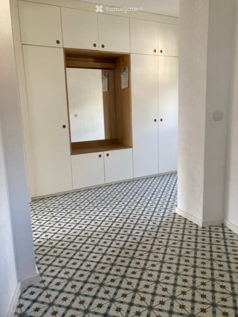 Empty room with white built-in wardrobes and a patterned tile floor.