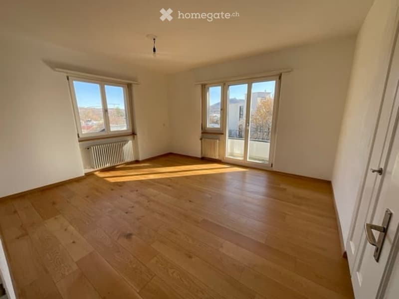 Empty room with wooden flooring, large windows, and radiators. No furniture or equipment present.