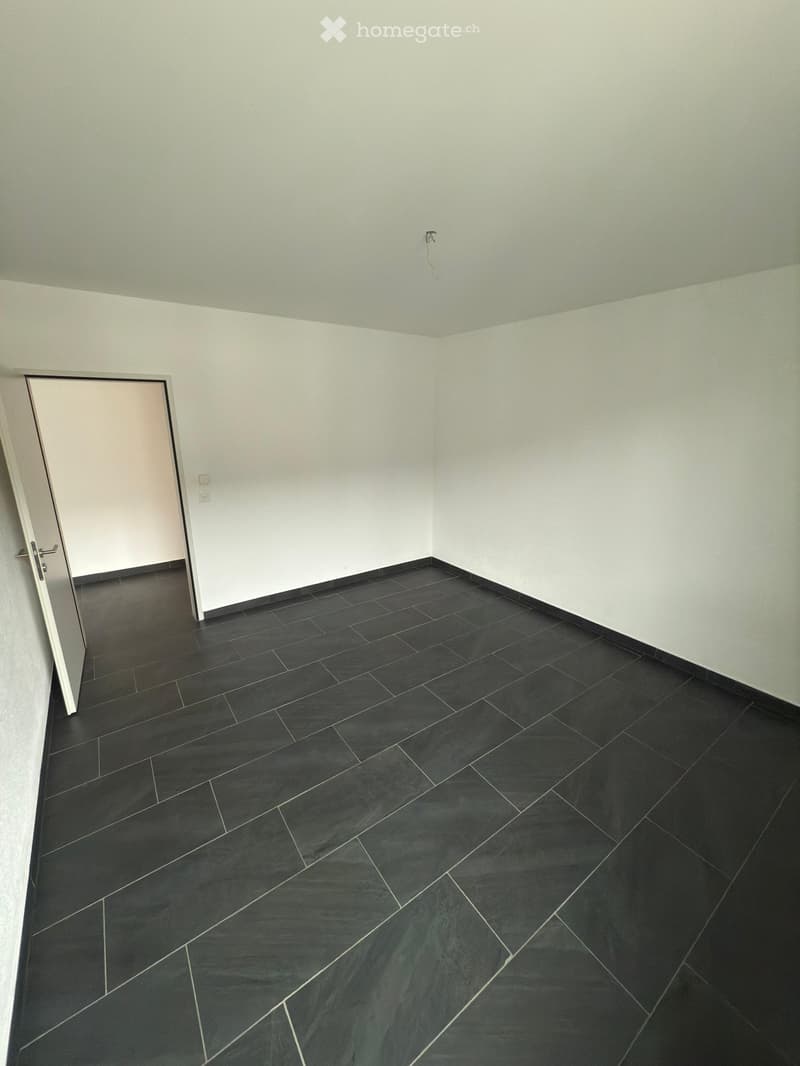 Empty room with light grey walls, black tiled floor, and a white door frame visible on the left side.