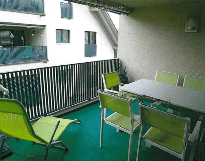 Balcony with green flooring, metal railing, and outdoor furniture including a table and chairs.