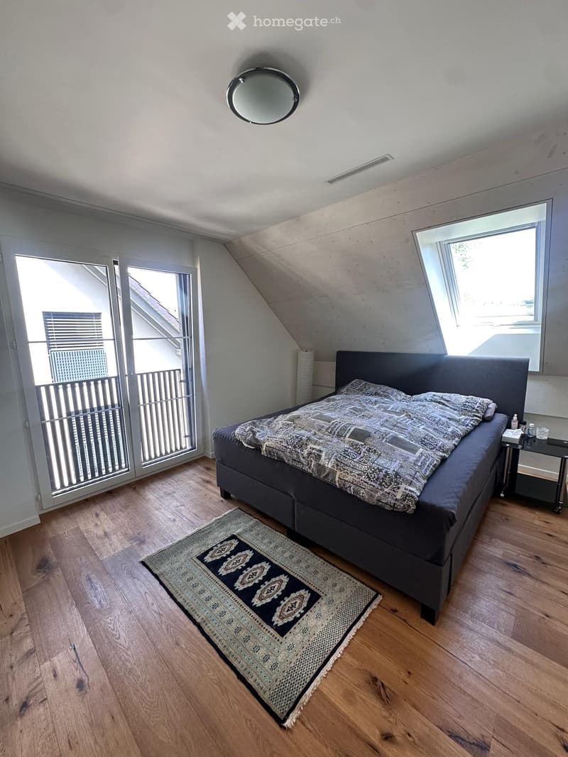 Bedroom with wooden flooring, large bed with dark headboard, patterned rug, nightstand, and round mirror on the ceiling.