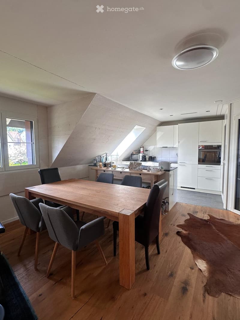 Modern dining area with a wooden dining table and chairs, integrated kitchen with white cabinets, microwave, refrigerator, and oven, and a small bar area with stools.