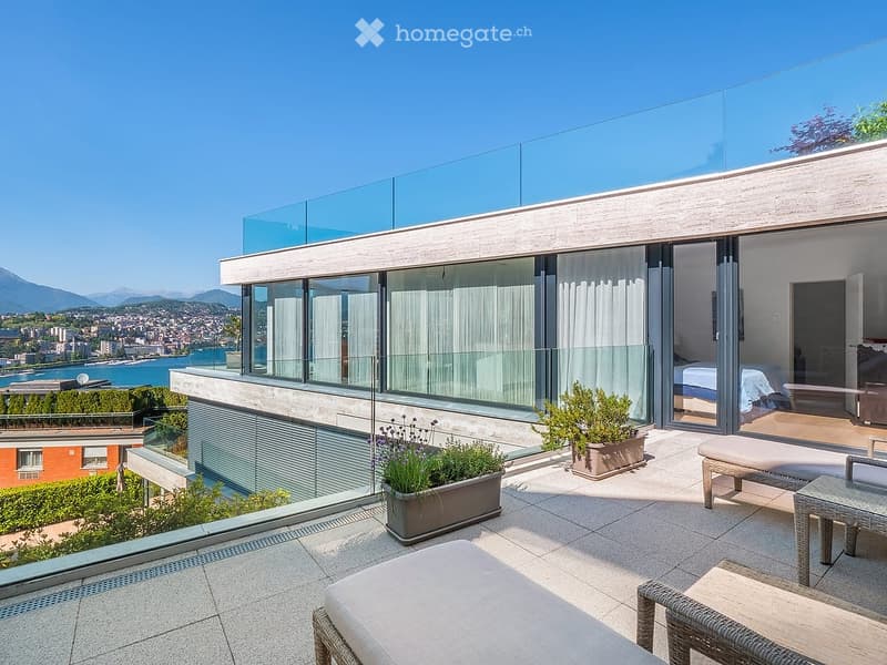 Modern rooftop terrace with panoramic city and lake view, featuring a glass railing, outdoor seating area with a table, chairs, and a bench, along with potted plants.