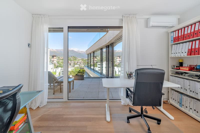 Modern office space with large windows offering a scenic mountain view, equipped with a desk, office chair, and shelving unit.