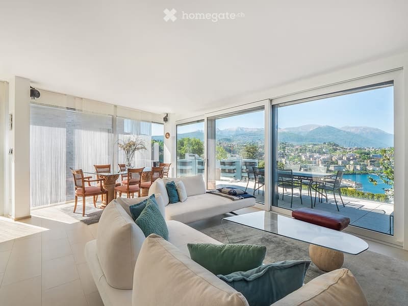 Modern living room with large windows offering a scenic view, featuring a white sofa, coffee table, dining area with chairs, and decorative vase.
