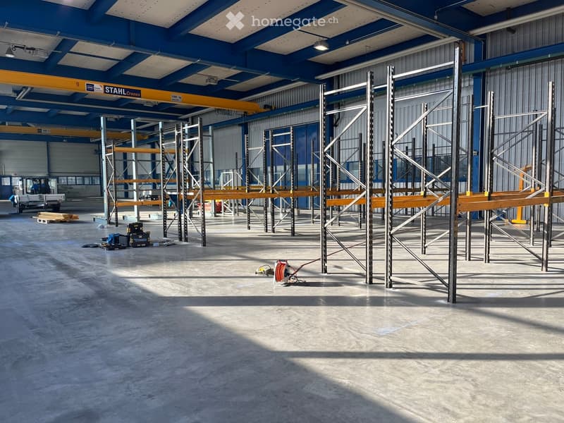 large warehouse with high ceiling, metal shelves and racks, open floor plan, grey concrete flooring
