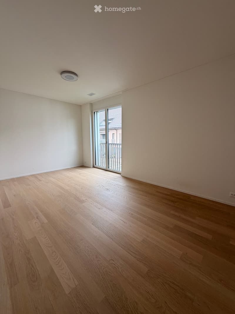 Empty room with light wooden flooring and white walls, featuring a large sliding glass door leading to a balcony.