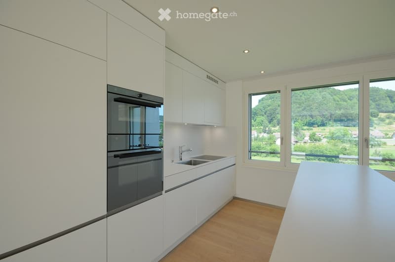 Modern kitchen with white cabinets, a built-in oven, a sink with a faucet, and a large window overlooking a green landscape.
