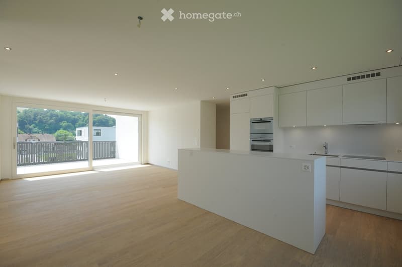 Modern kitchen with white cabinets, stainless steel appliances, and a central island. Large windows provide natural light and a view of the outdoor area.