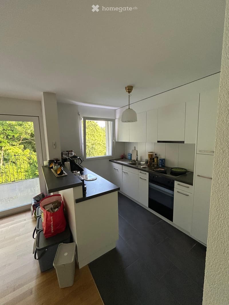 Modern kitchen with white cabinets, dark countertops, and stainless steel appliances. Features an island with a sink, stove, and various kitchen items.