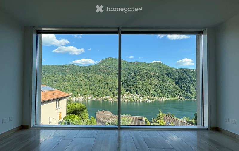 Empty room with large floor-to-ceiling windows offering a scenic view of a lake and surrounding hills.