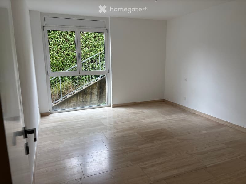 Empty room with light wooden flooring, white walls, and a large sliding glass door leading to a staircase and outdoor area.