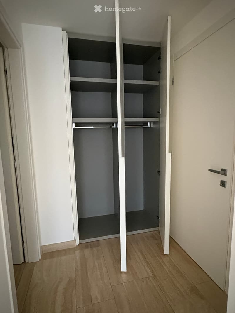 Empty hallway with wooden flooring and white walls, featuring two open wardrobes with empty shelves and hanging space.