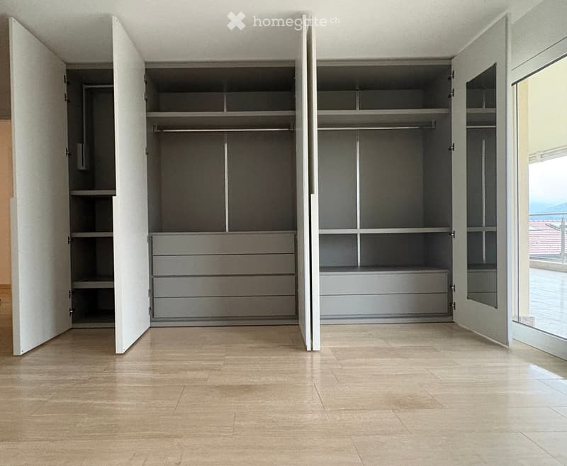 Empty room with light-colored wooden flooring and large built-in closet units with open shelving and drawers.