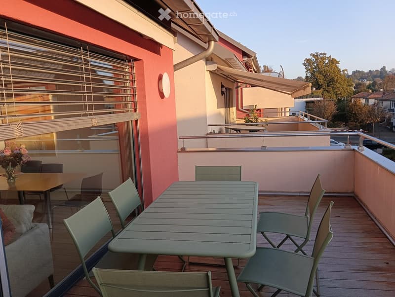 Balcony with wooden decking, outdoor table and chairs, sofa, and a view of the surrounding area.