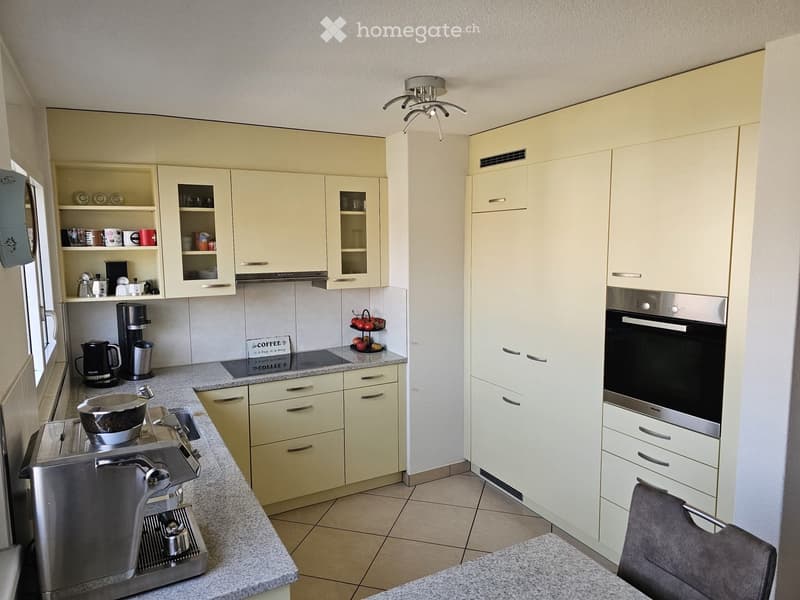 modern kitchen with tiled floor, yellow cabinets, granite countertops, ceiling light, stove, oven, dishwasher, coffee machine, and various kitchenware