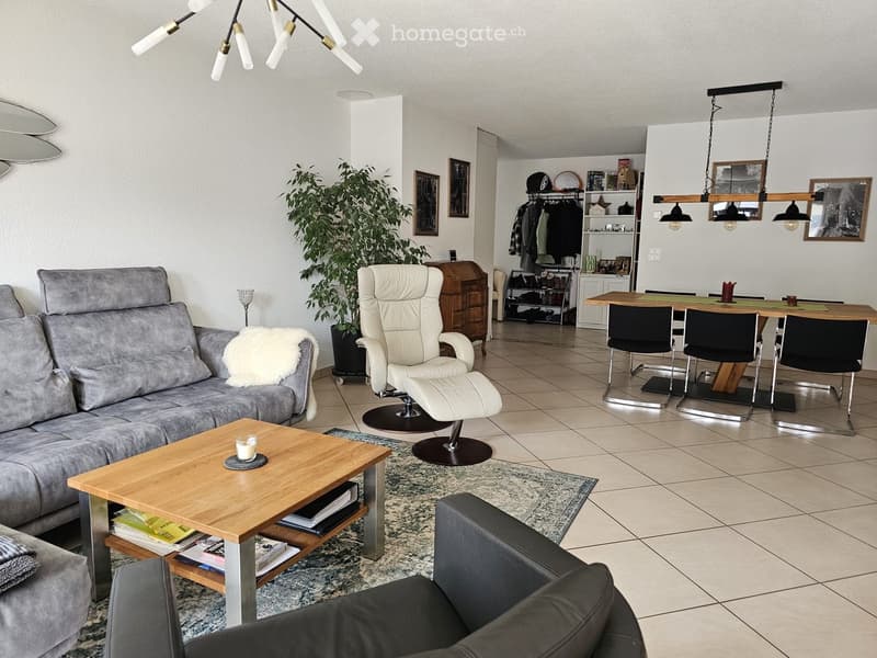 Sofa, coffee table with books, white reclining chair, dining table with chairs, plant, wooden floor, white walls