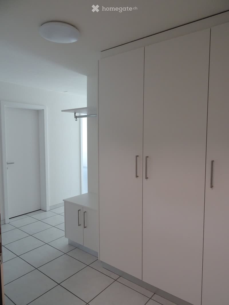 Empty room with white tiled floor, white walls, built-in cabinets, and a small shelf. No furniture or personal items present.