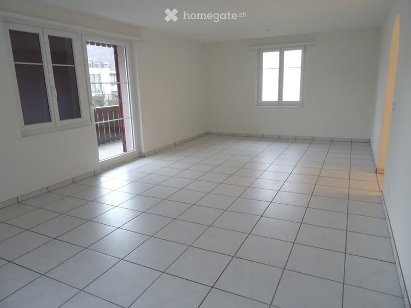 Empty room with white tiled flooring, white walls, and large windows, including a sliding glass door leading to a balcony.