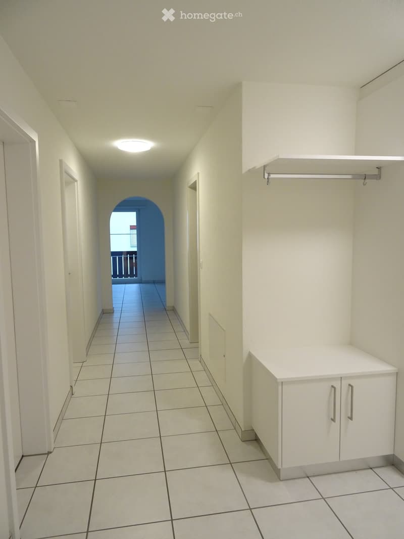 Empty hallway with white walls, tiled floor, built-in white cabinetry, and a recessed ceiling light. An arched doorway leads to a balcony area.