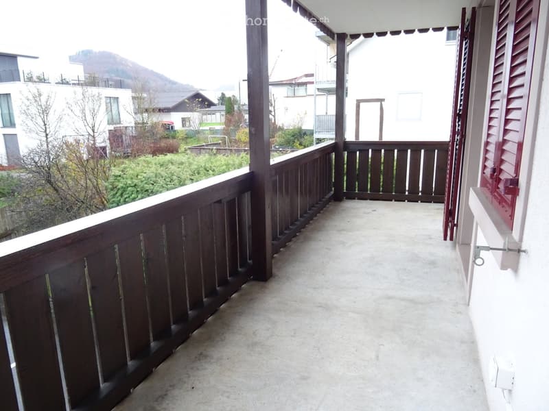 Balcony with wooden railing, concrete floor, and scenic mountain view in the background.