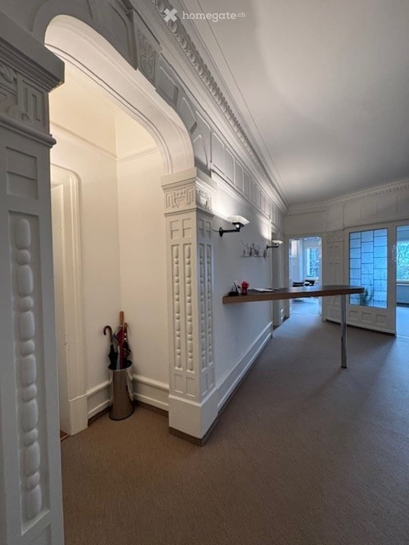 empty hallway, white walls, large windows, carpeted floor, table with items, umbrellas in a bin