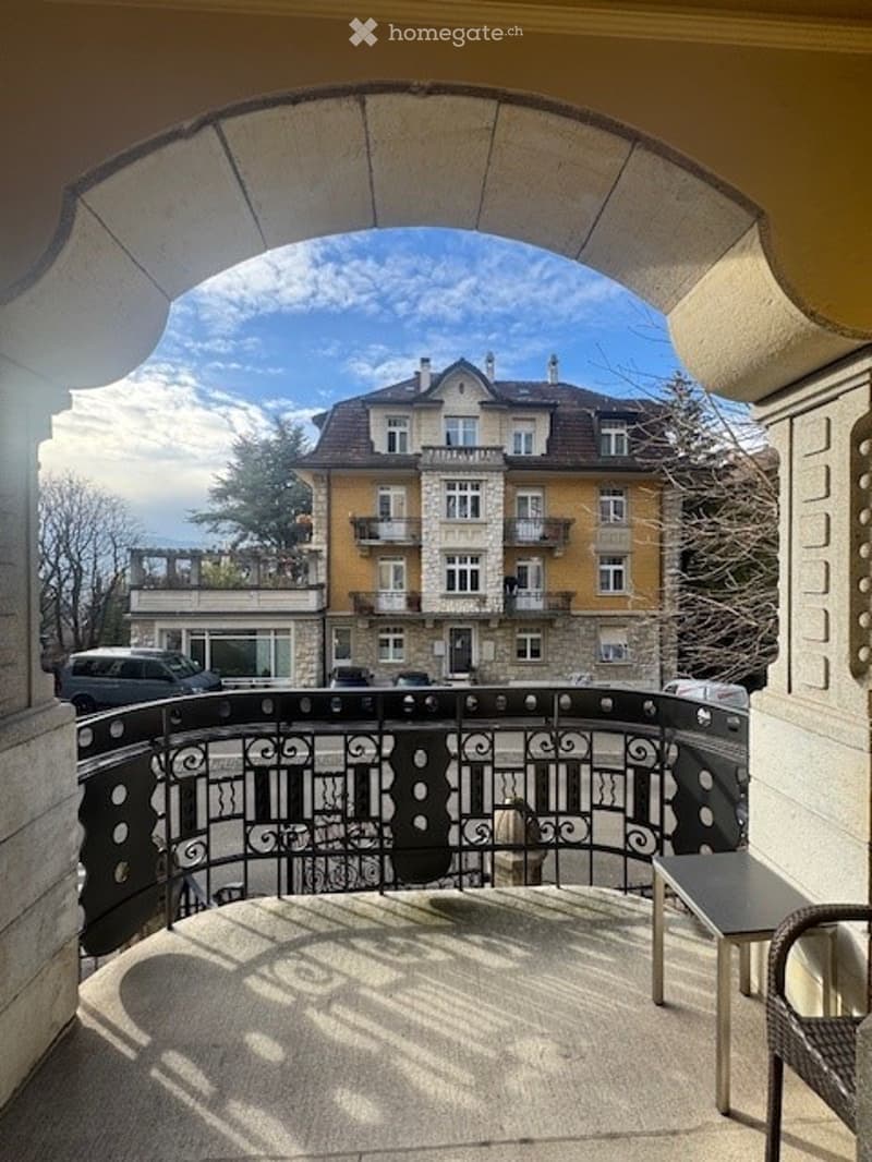 Balcony with railing, small table, car parked outside, building in background