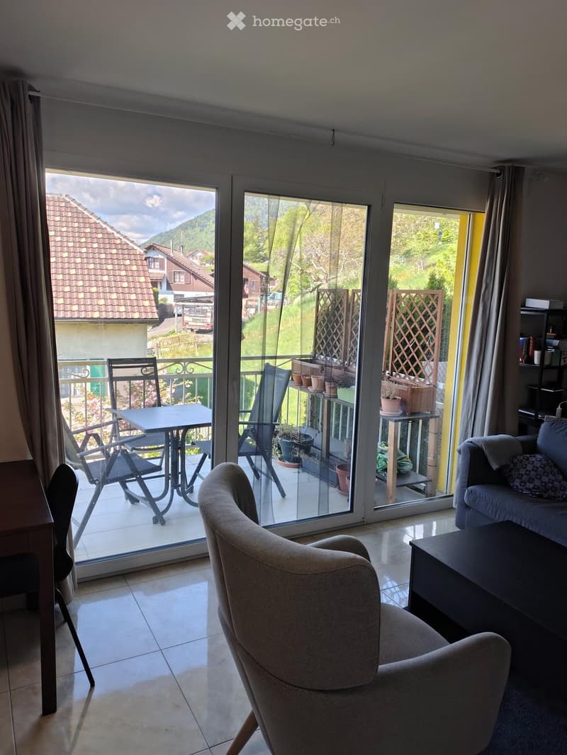 Living room with a sofa, coffee table, and a balcony with outdoor furniture including a table and chairs.