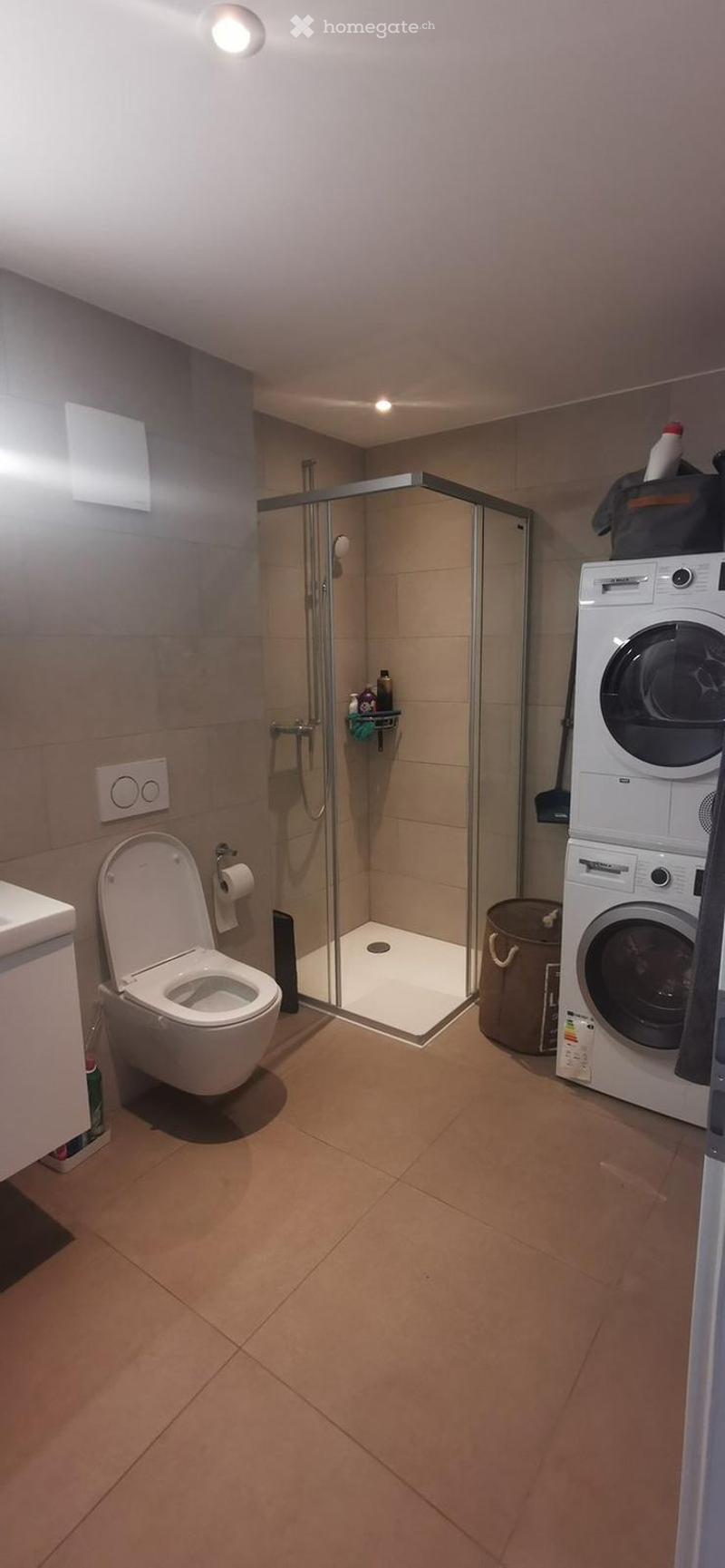 Modern bathroom with a toilet, glass-enclosed shower, washing machine, and light fixtures.