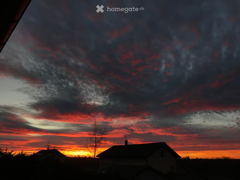 A house silhouette against a dramatic sunset sky with red and orange hues, featuring a chimney and a small tree in the foreground.