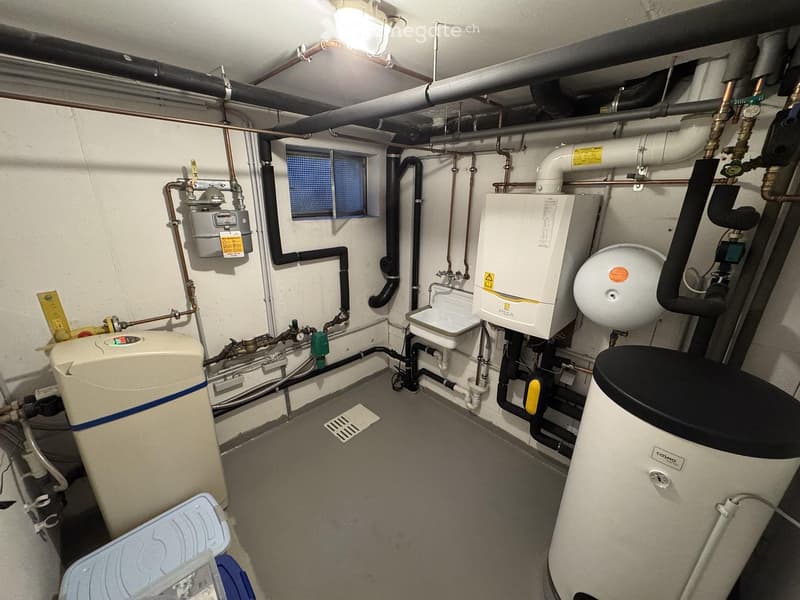 Utility room with water heater, boiler, pipes, valves, and a window for ventilation.