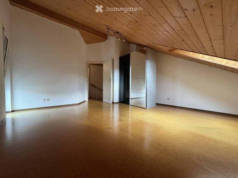 Empty room with wooden floor and white walls, featuring a closet with mirrored doors and a slanted wooden ceiling with recessed lighting.