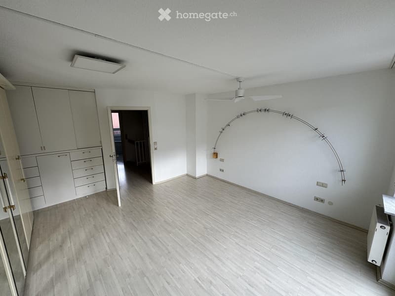 Empty room with light wooden flooring, white walls, built-in closet, and a curved floor lamp. No furniture or personal items are present.