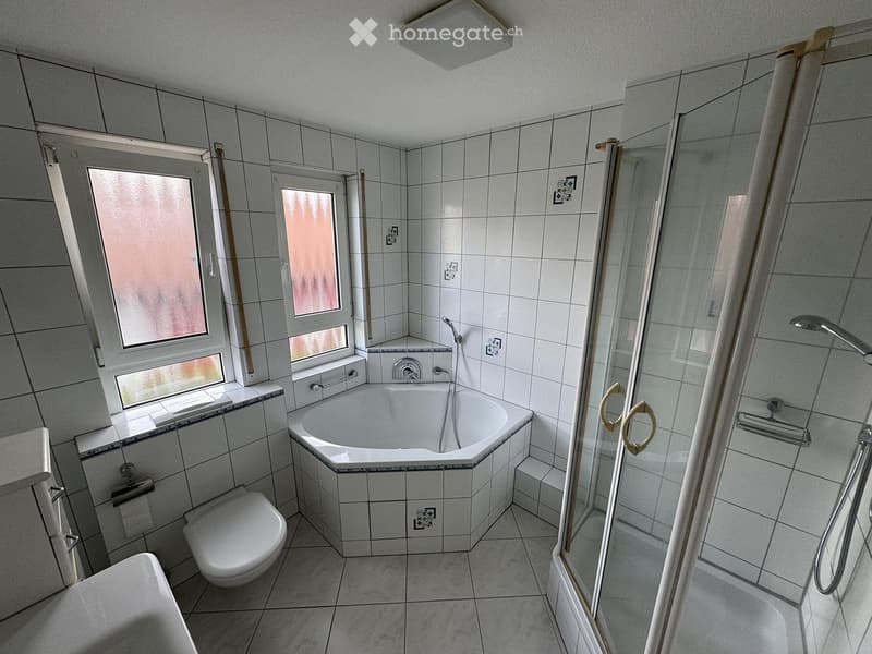 Bathroom with a bathtub, toilet, shower, and window with frosted glass. The walls and floor are tiled in white.