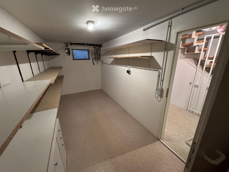 Empty basement or storage area with built-in wooden shelves, a small window, and a staircase leading to another area.