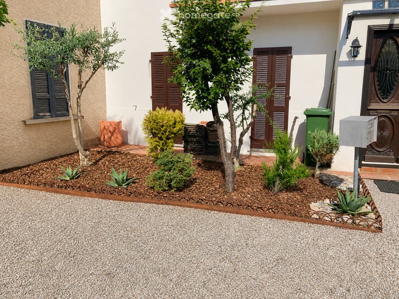 Well-maintained garden area with gravel, small trees, shrubs, and decorative elements near a house entrance.