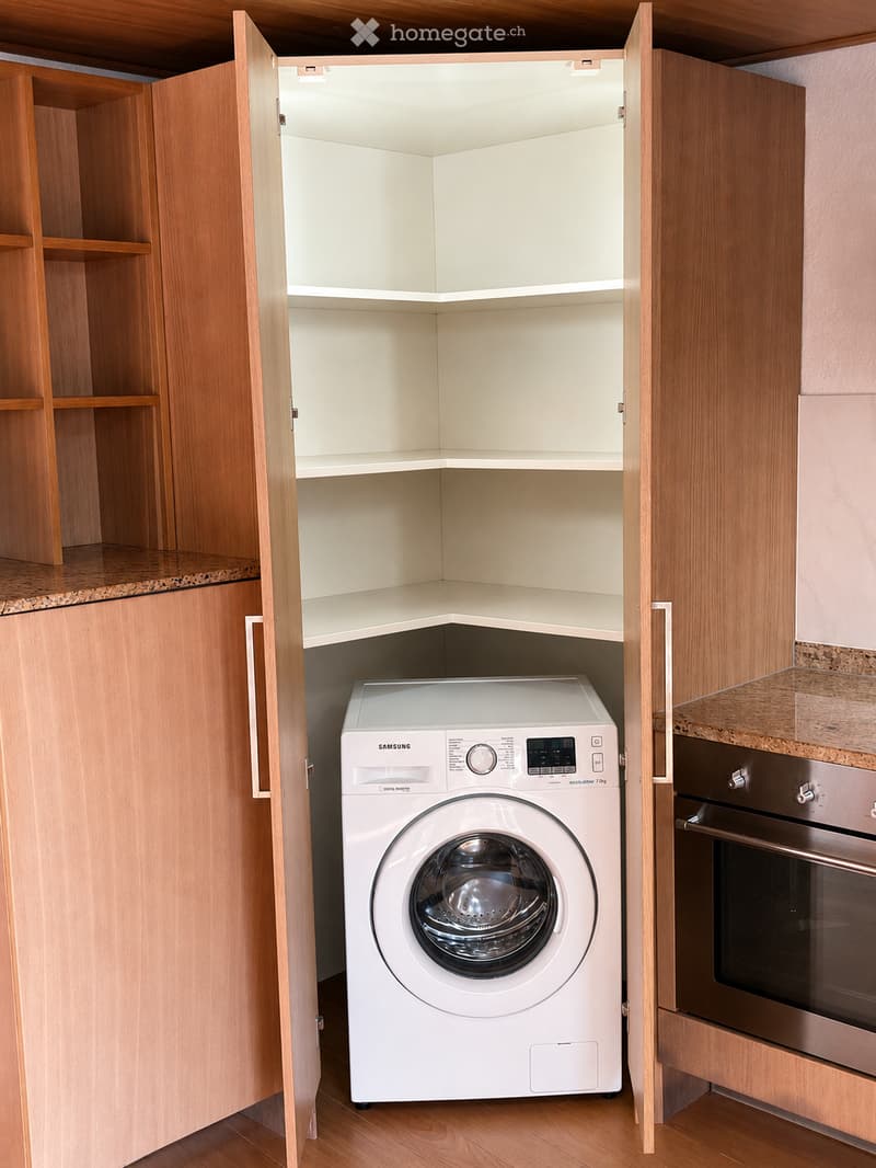 Modern bathroom with a corner cabinet, a white Samsung washing machine, and a stainless steel oven.