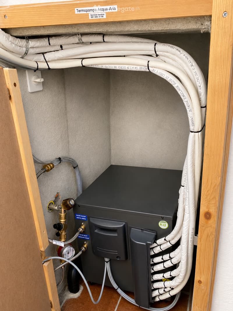 A water pump unit with multiple white pipes, valves, and a pressure gauge installed in a wooden cabinet.