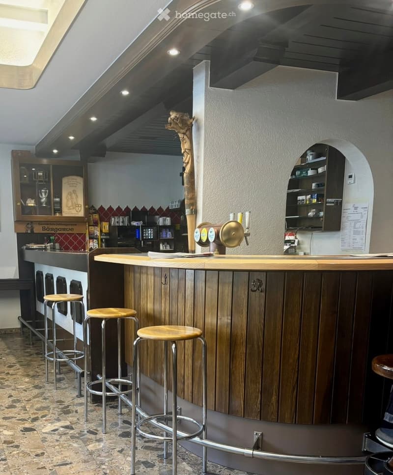 A stylish bar area with a wooden counter, several bar stools, a faucet, and shelves stocked with various items.