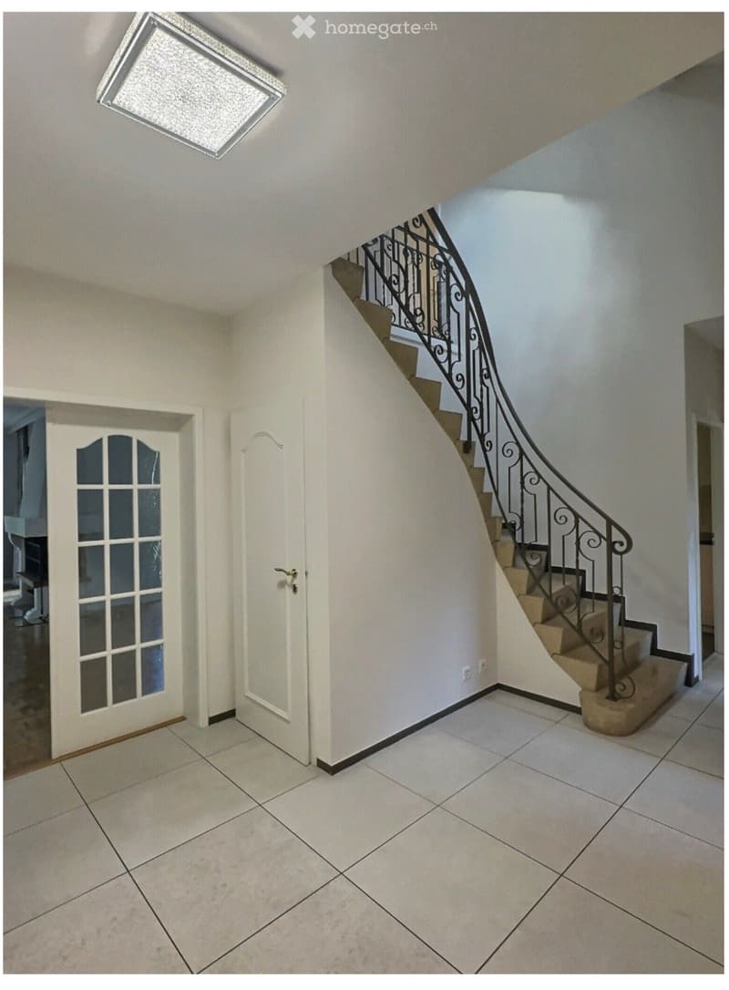 Hallway with tiled floor, white walls, staircase with metal railing, and a frosted glass door leading to another room.