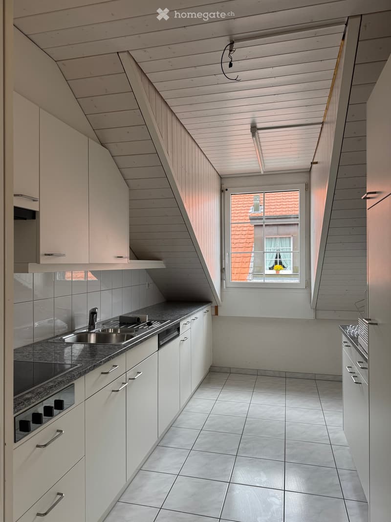 Modern kitchen with white cabinets, stainless steel sink, oven, and dishwasher. Grey tiled floor and countertops.