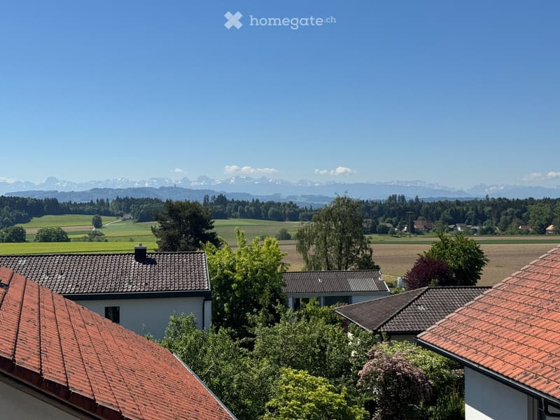Residential houses with red-tiled roofs, surrounded by lush greenery and a scenic mountain backdrop.