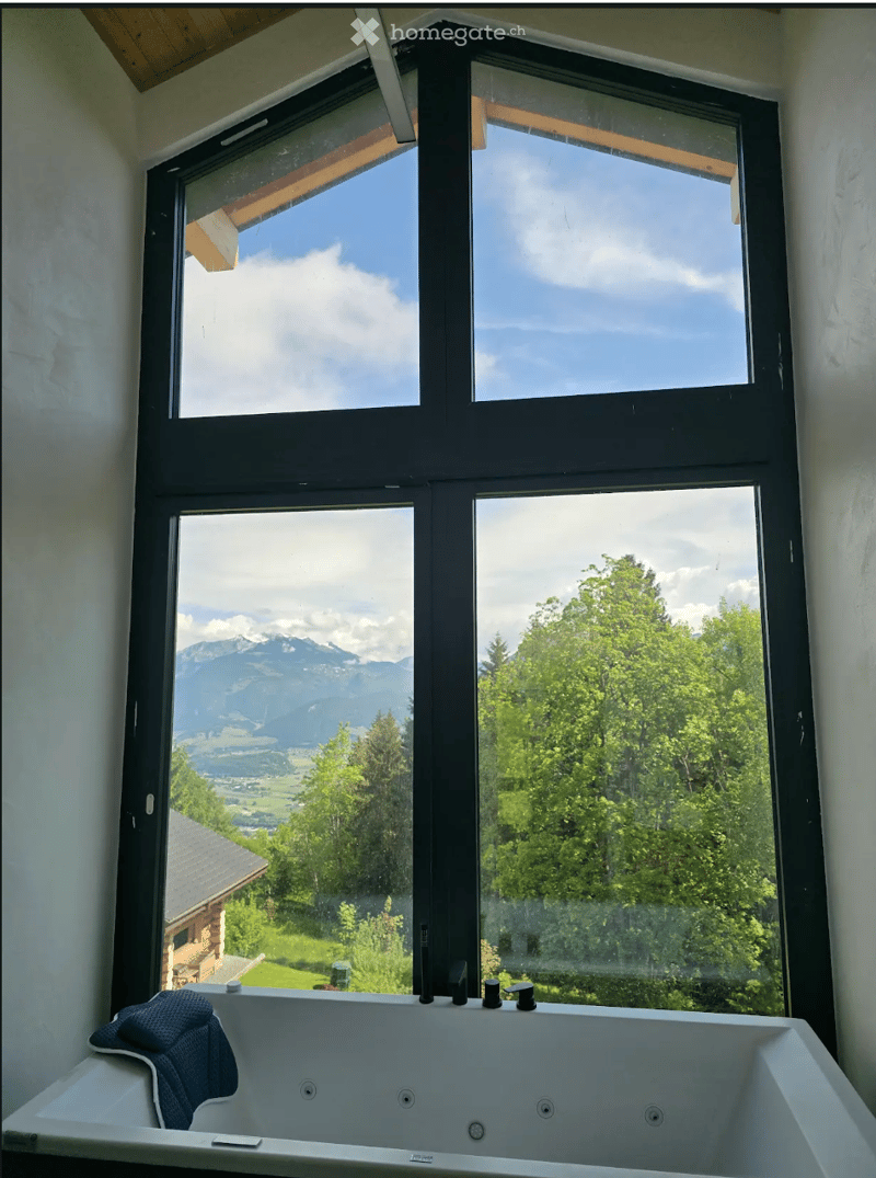 Bathroom with a large window offering a scenic mountain and valley view, featuring a modern bathtub with a towel draped over the edge.