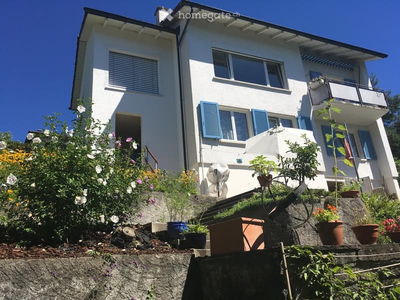 two-story house, white painted exterior, blue shutters, balcony, plants, raised ground floor